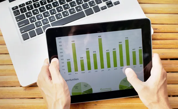 Person's hands holding a tablet with a bar chart on the screen 