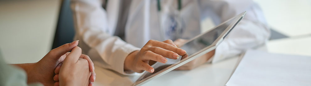 Close up of a doctor looking at a tablet screen with a patient 