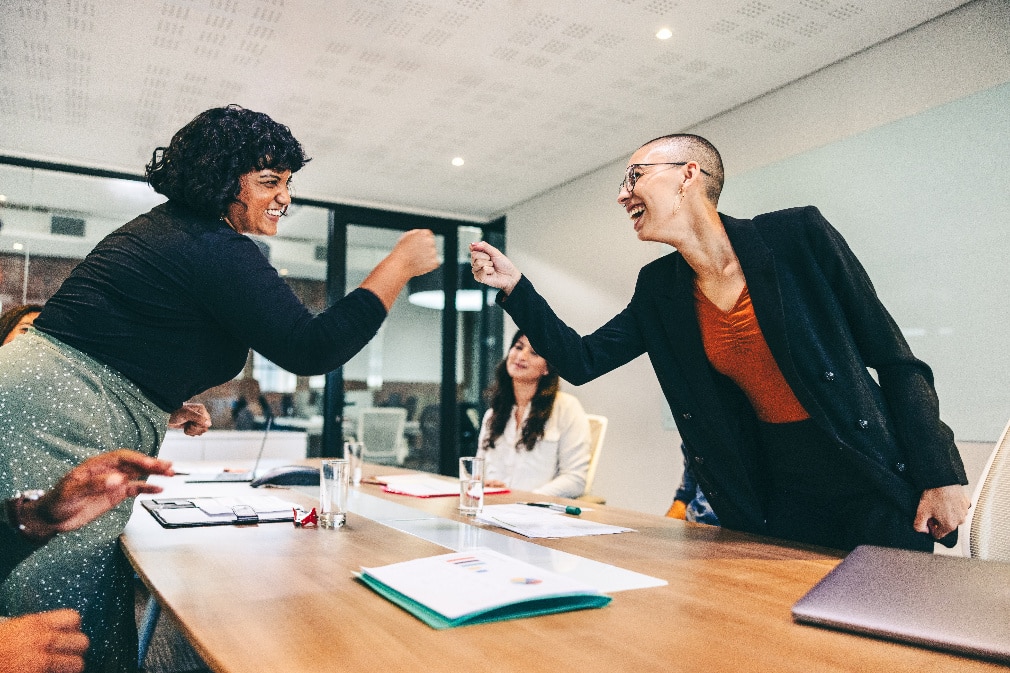 two women fist bump across a conference table