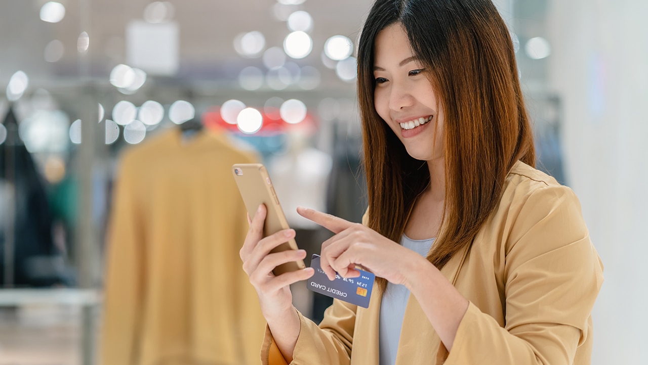 Kunde bruker mobiltelefon og betalingskort under shopping Kunde bruker mobiltelefon og betalingskort under shopping