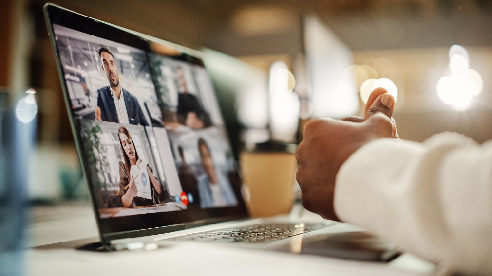 a man on his laptop in a zoom meeting with the participants on the screen