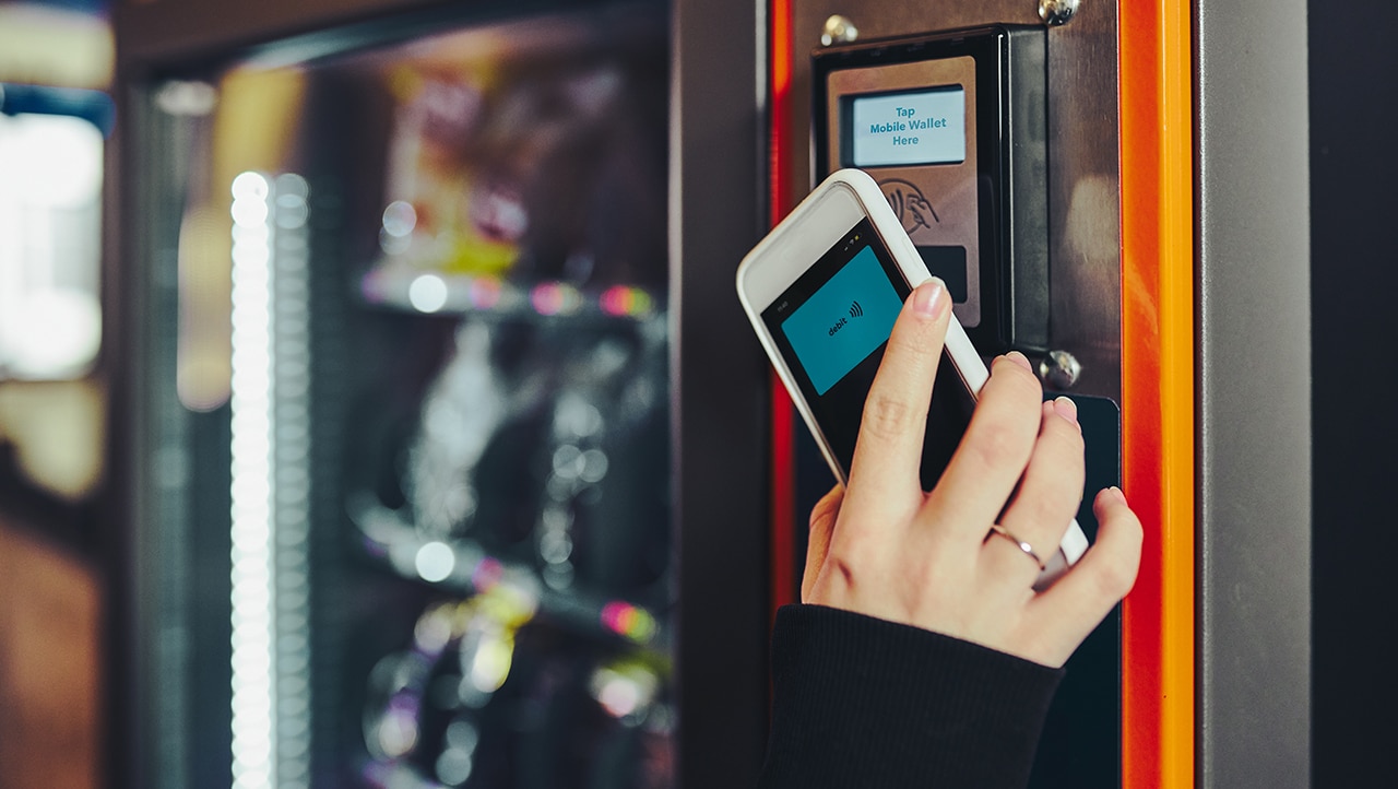 Person betaler kontaktløst med mobiltelefon ved en betalingsterminal. Person betaler kontaktløst med mobiltelefon ved en betalingsterminal.