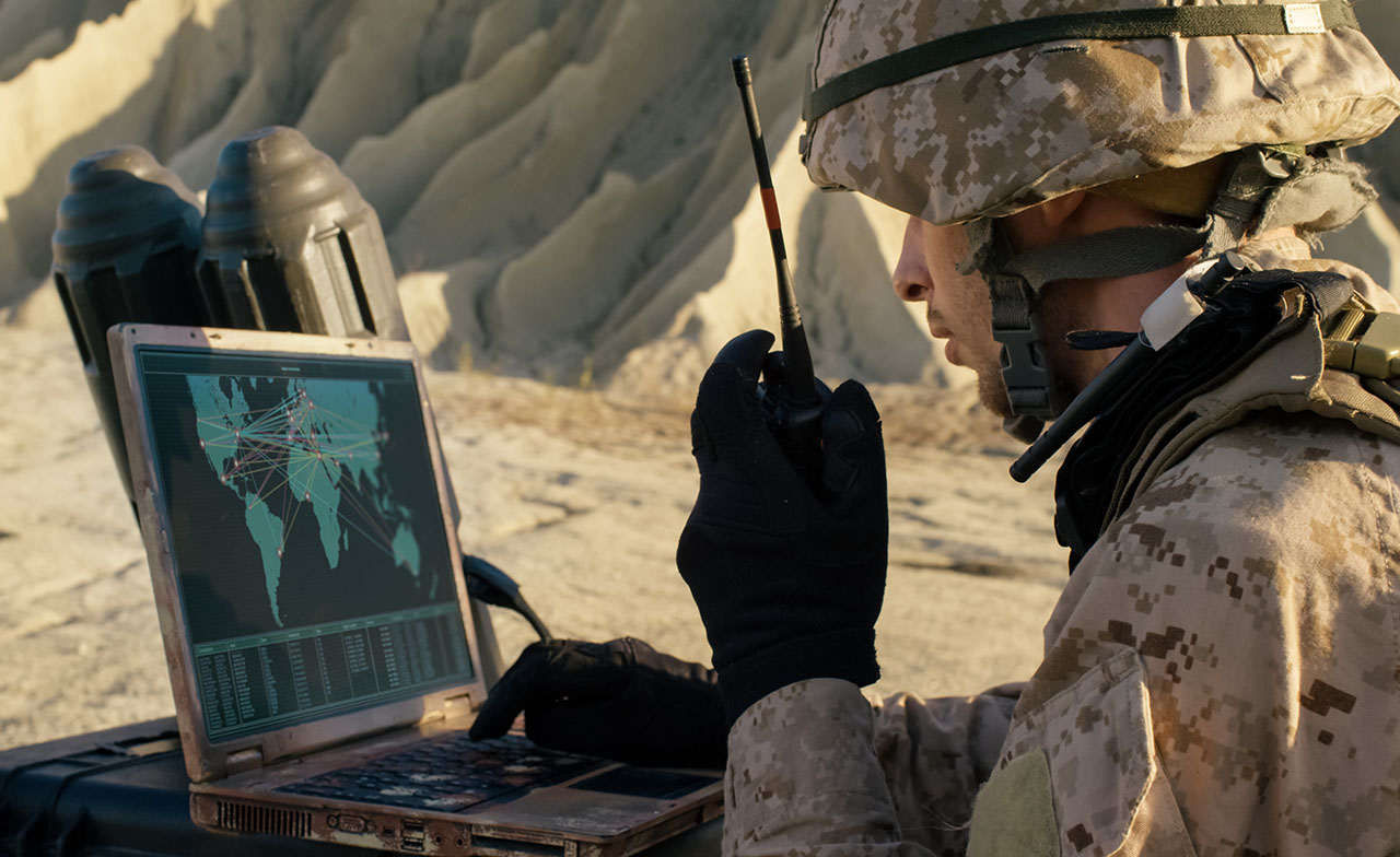 Soldat utilisant un ordinateur portable et une radio pour communiquer pendant une opération militaire dans le désert