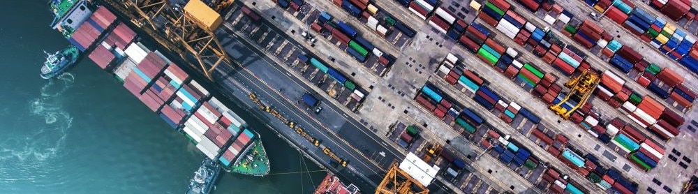 Draufsicht auf einen Hafen mit Frachtschiff und gestapelten Containern, Logistik und globaler Warenverkehr