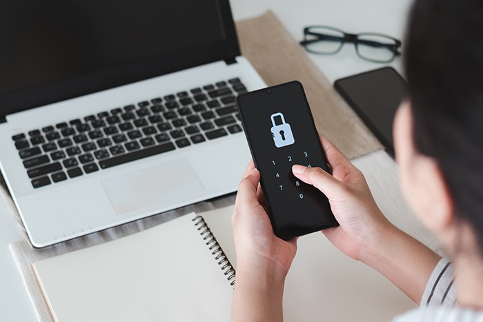 professional in front of laptop holding a mobile device with a lock on the screen