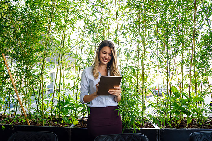 woman standing in front of greenery looking at an ipad 