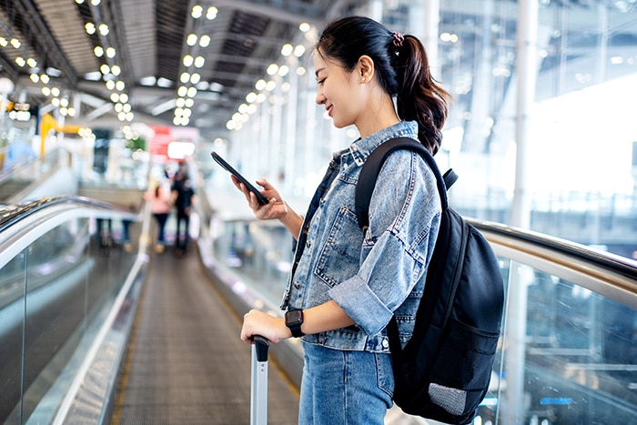 Asian woman tourist in casual clothes using a smartphone on escalator at airport terminal