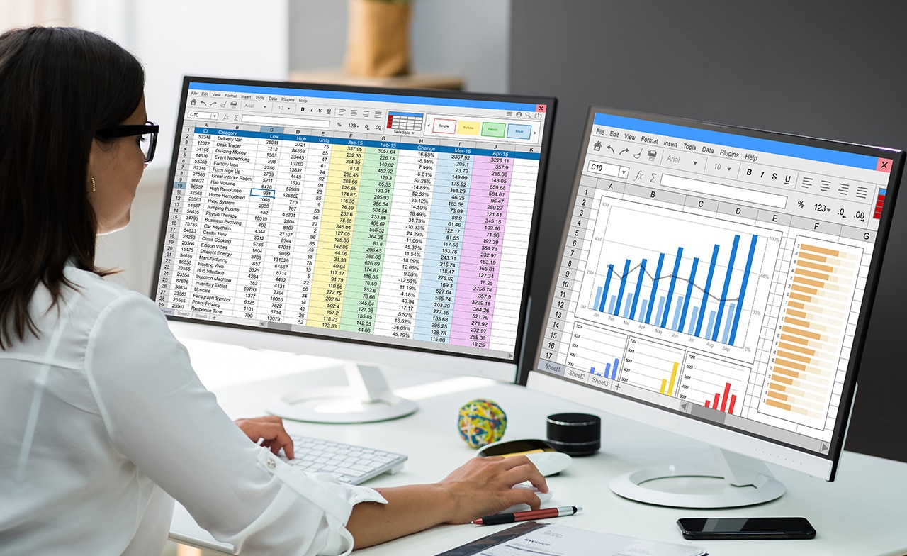 Person arbeider med regneark og grafer på to skjermer ved skrivebord. Person arbeider med regneark og grafer på to skjermer ved skrivebord.