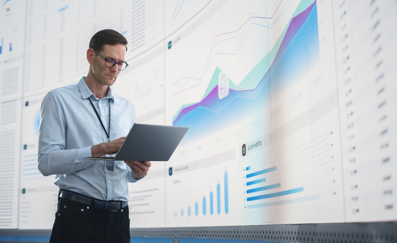 Manager analysiert interaktive Datenvisualisierungen auf großem Dashboard zur KI-gestützten Auswertung von Fahrzeug- und Marktdaten.