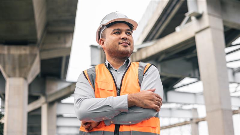 Asian man wearing a safety helmet and neon orange reflective jacket