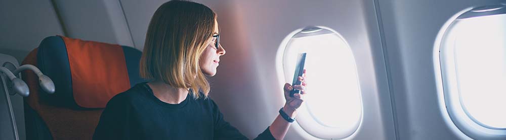 Femme d’affaires prenant une photo avec son smartphone à bord d’un avion Femme d’affaires prenant une photo avec son smartphone à bord d’un avion