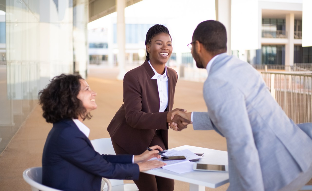 Business people meeting around a desk. Two smiling and standing shaking hands