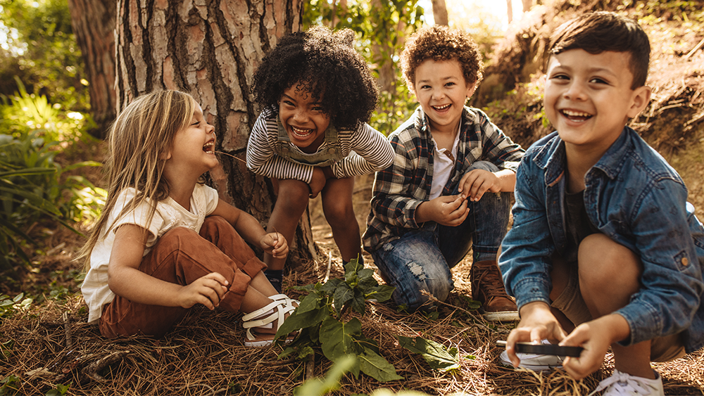 Smiling happy children sitting in a forest around a a tree sapling