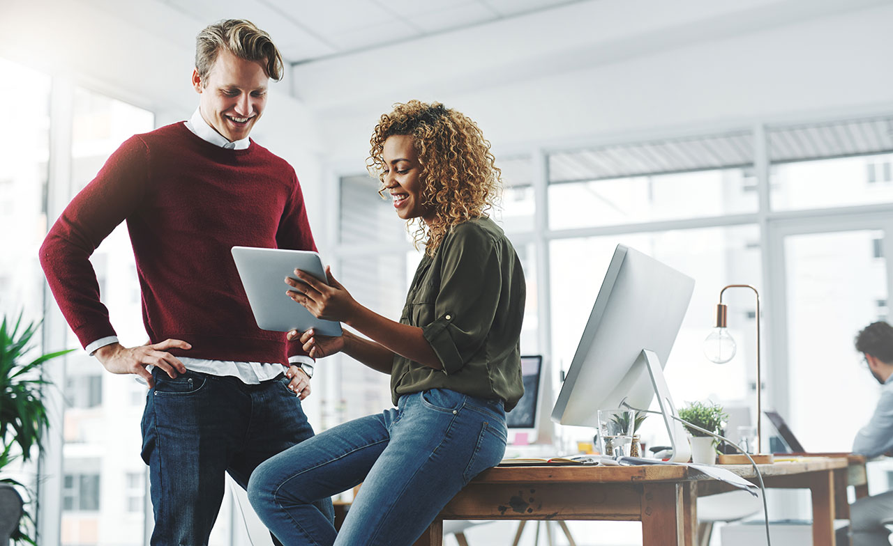 Två kollegor i ett modernt kontor samarbetar och tittar tillsammans på en surfplatta.