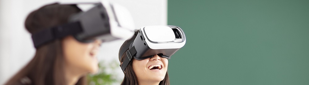 Två skolelever sitter skrattande med VR-glasögon i ett klassrum
