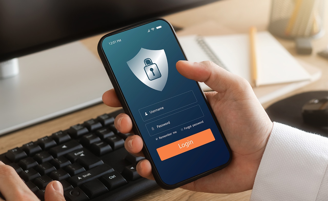 Person holder mobil med innloggingsskjerm og låsesymbol foran tastatur.