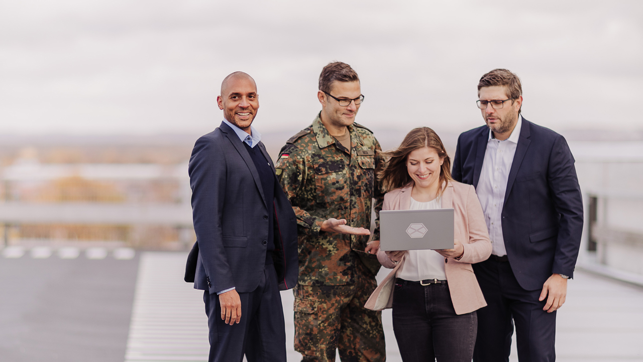 Vier CGI Member stehen draußen zusammen, eine Person trägt eine Bundeswehr-Uniform