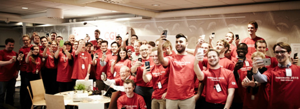 En stor grupp av CGI medarbetare med röda t-shirts under CGI InMoment i Göteborg står med sina mobiler och tar selfie-bilder i storgrupp