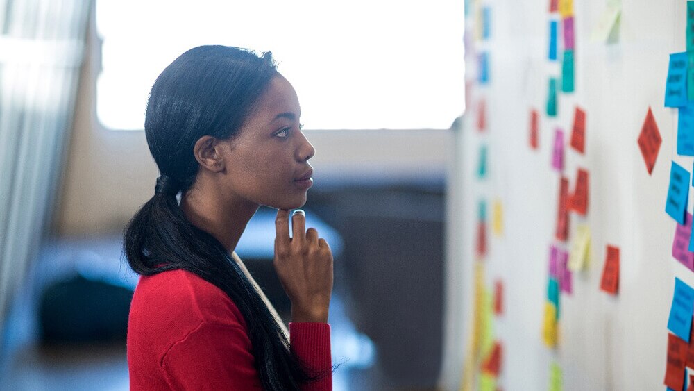 Frau steht vor einem Whiteboard mit vielen bunten PostITs