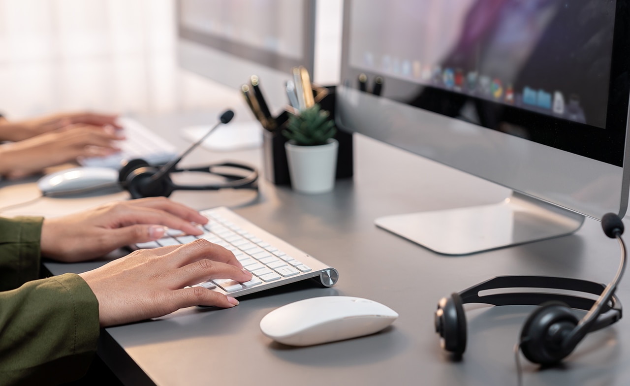 Person som jobber på helpdesk forran PC og med headset liggende ved tastaturet