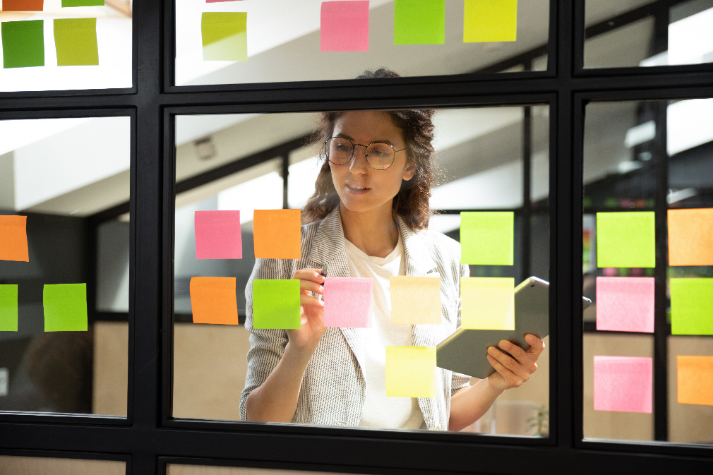 person adding post-it notes to transparent agile board