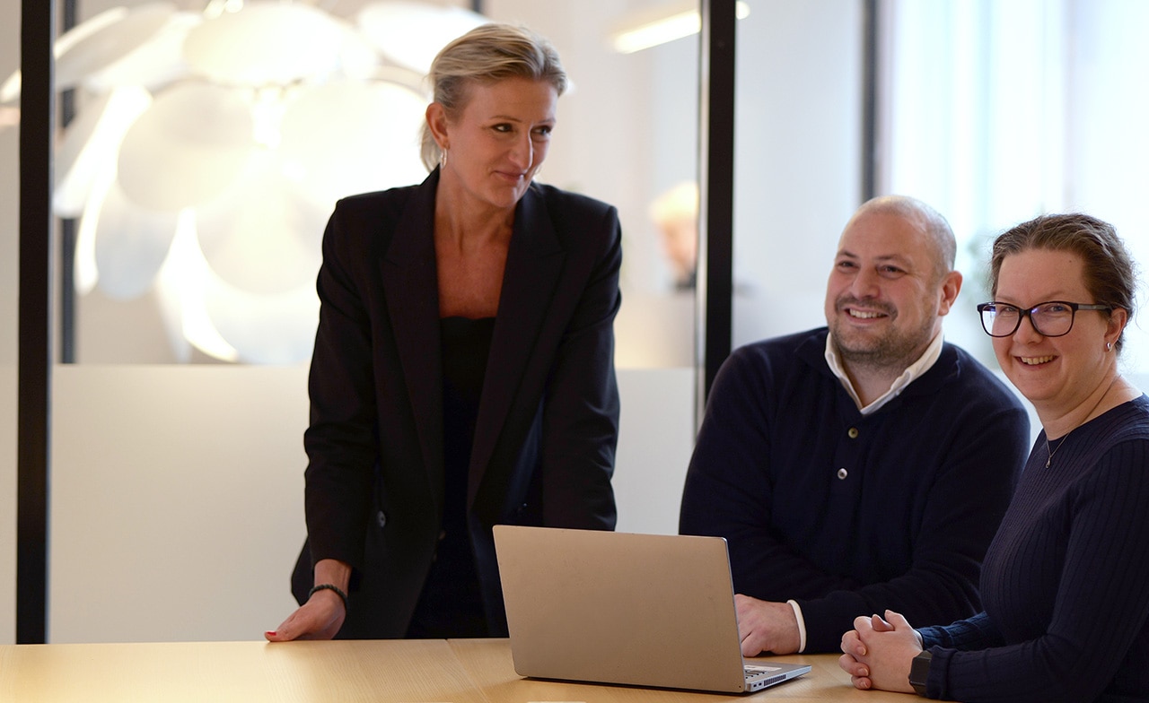 Tre personer i møte rundt laptop ved bord i kontormiljø Tre personer i møte rundt laptop ved bord i kontormiljø