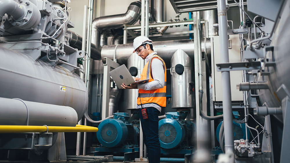 man working in utility plant holding laptop