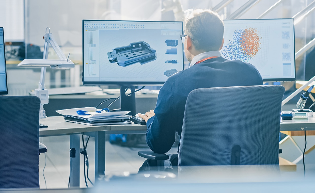 Person jobber med 3D-modellering og datavisualisering på to skjermer i kontormiljø.