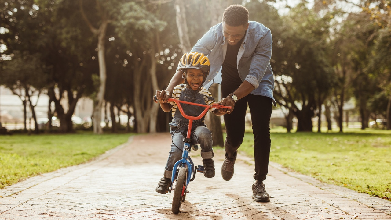 father helping child learn to ride a bike