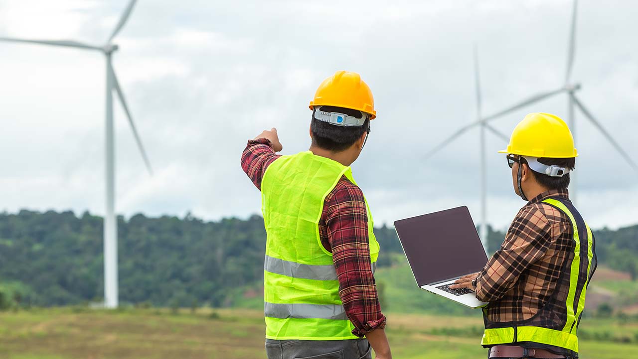 two workers in hard hats and hi-vis vests point at wind turbine