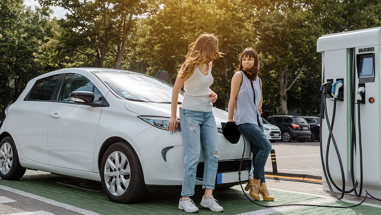 2 women leaning against electric car whilst it is charging