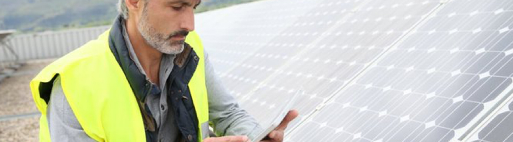 Energy engineer wearing an helmet works on his tablet next to solar panels