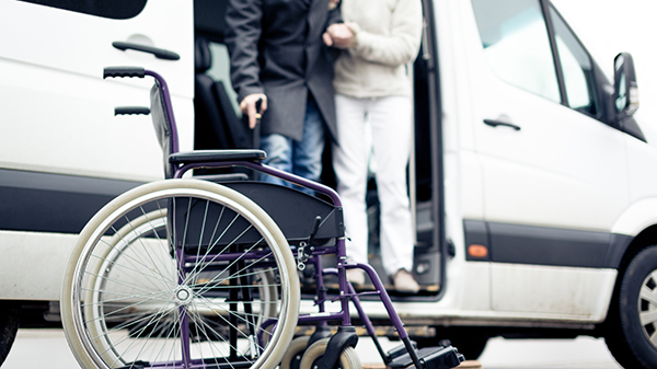 En pasient som hjelpes ut av en bil til en rullestol