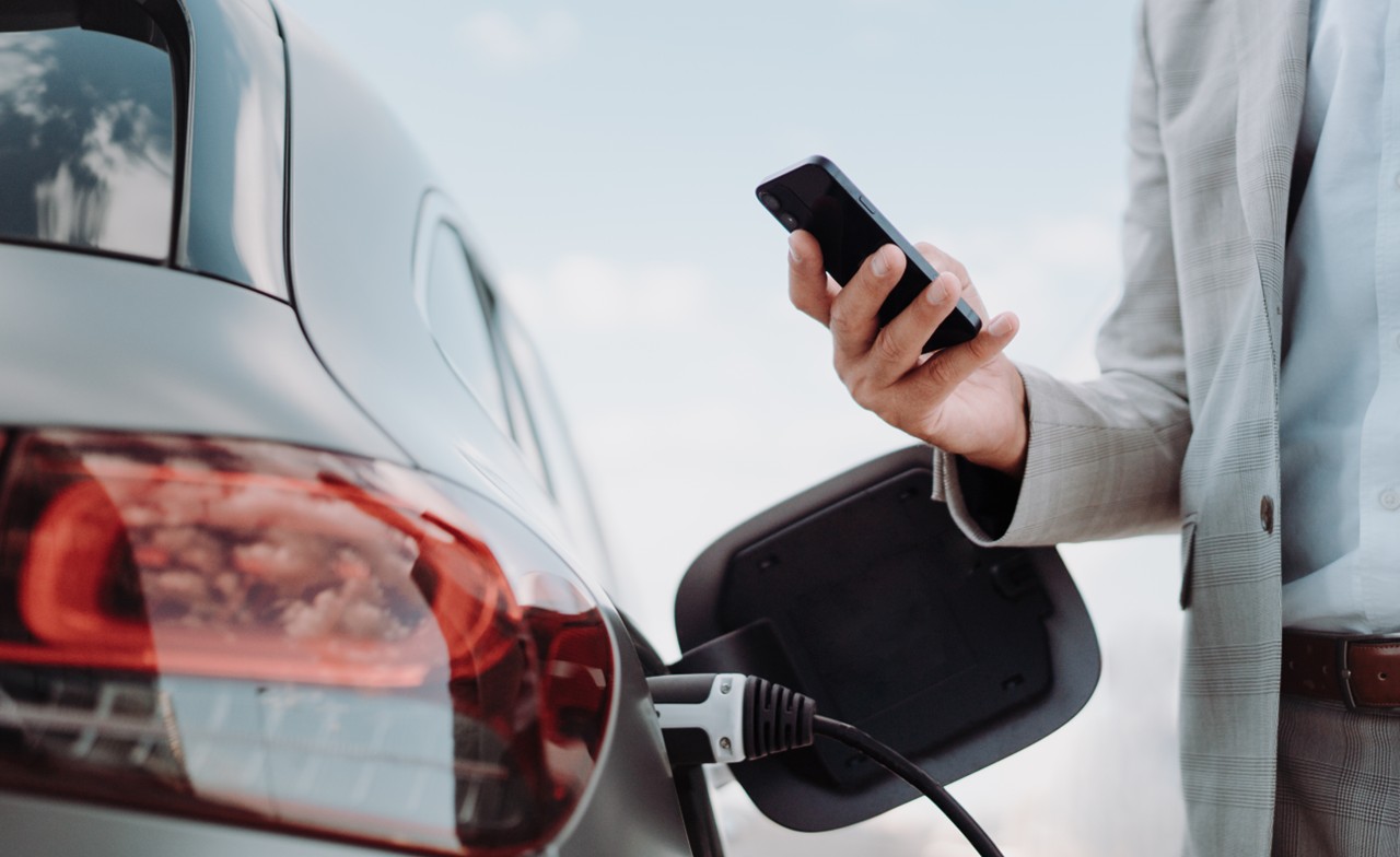 person-charging-car-530089254 A person charging his car and looking at a smartphone