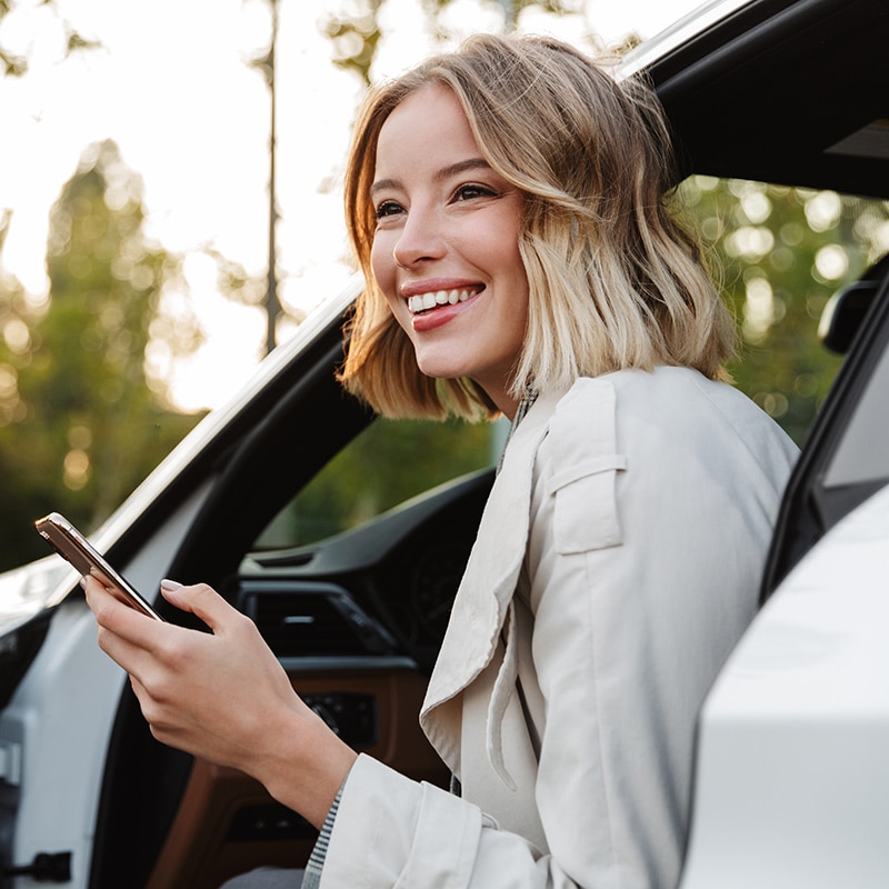Henkilö istuu ulkona autossa kännykkä kädessä