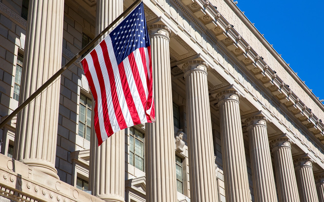 pqc-website-image-1 The American flag flying between government building pillars