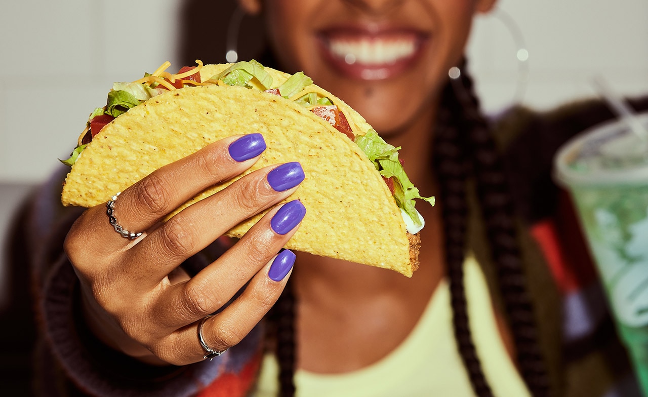 Henkilö näyttää Taco Bellin tacoa kädessä