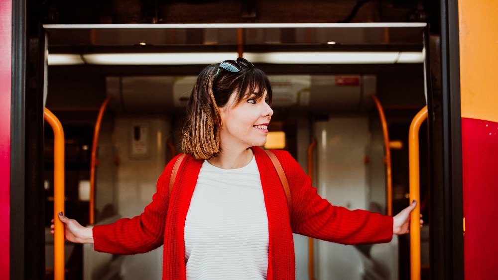 Smiling female train passenger ready to disembark through open doors of the train