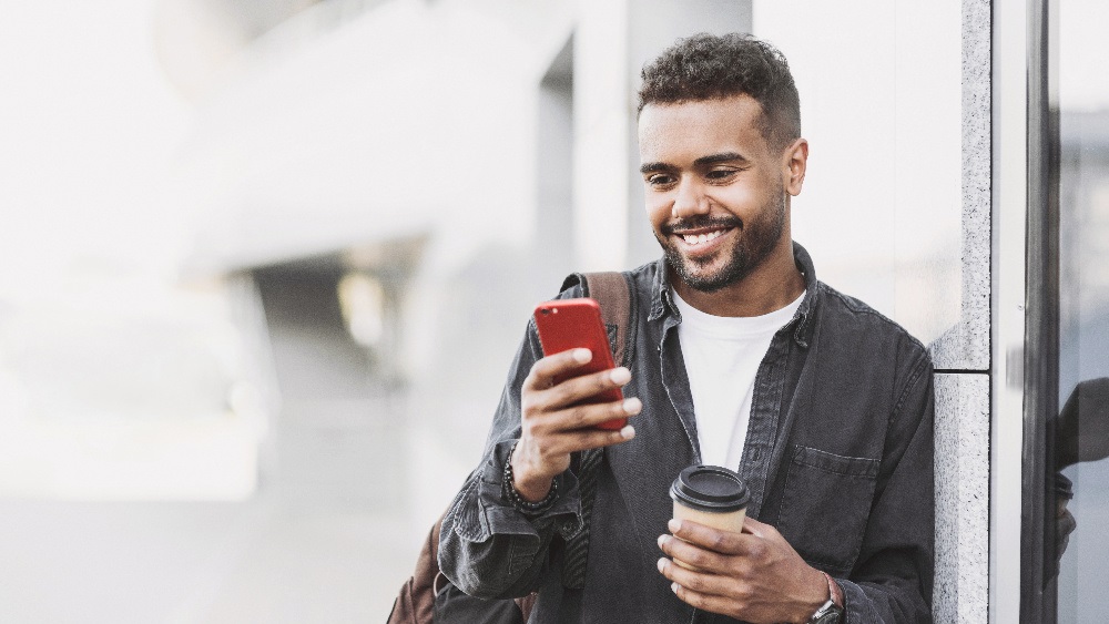 smiling man using phone and holding coffee cup