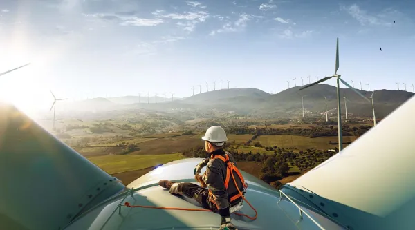 engineer sitting atop a wind turbine looking at a sunset landscape