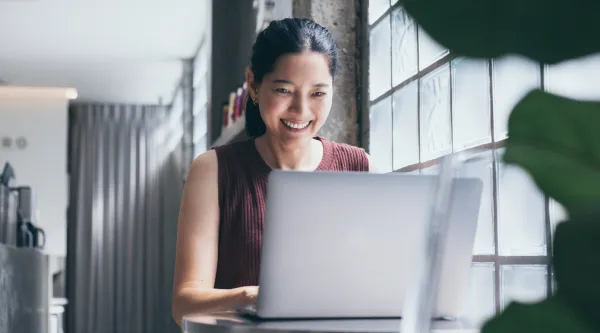 Kvinna arbetar på en dator och ler. 