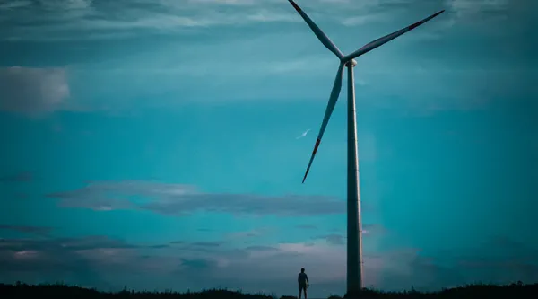 A wind turbine against a dark sky, a small silhouette of a man next to it