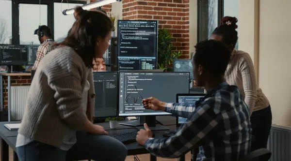 three professionals gathered around a computer looking at code