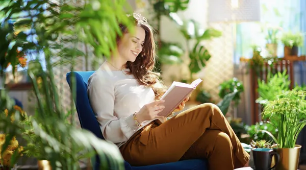 Frau sitzt in einem Zimmer mit vielen grünen Pflanzen und liest ein Buch