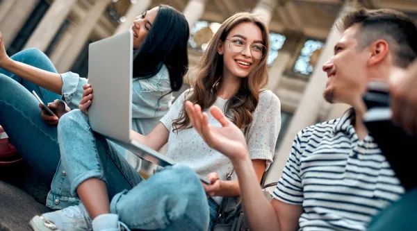 Group of students chat happily around a laptop