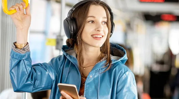 Kuvituskuvassa nuori nainen matkustaja seisoo kuulokkeiden ja älypuhelimen kanssa bussissa