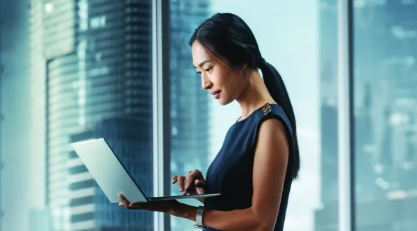 Female professional standing with laptop near office window