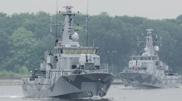 Två militärfartyg på öppet hav med skog och land i bakgrunden