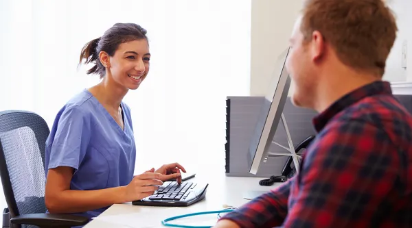 Nurse on a computer chatting to a patient in an office setting.