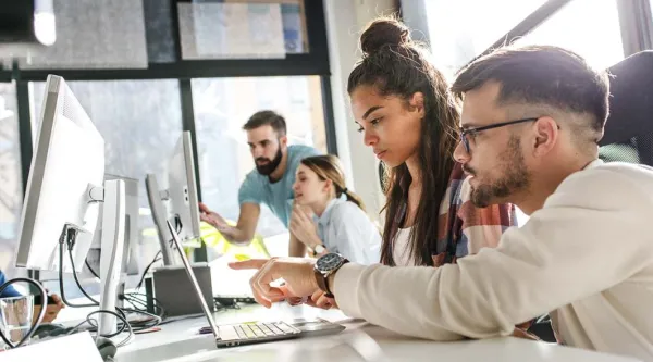 Co-workers working and talking in front of computer screens 
